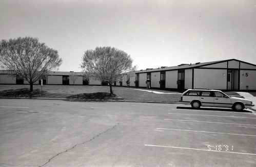 Barracks and parking area with man walking on sidewalk. Building number 5. [Image possibly for comparative housing study]