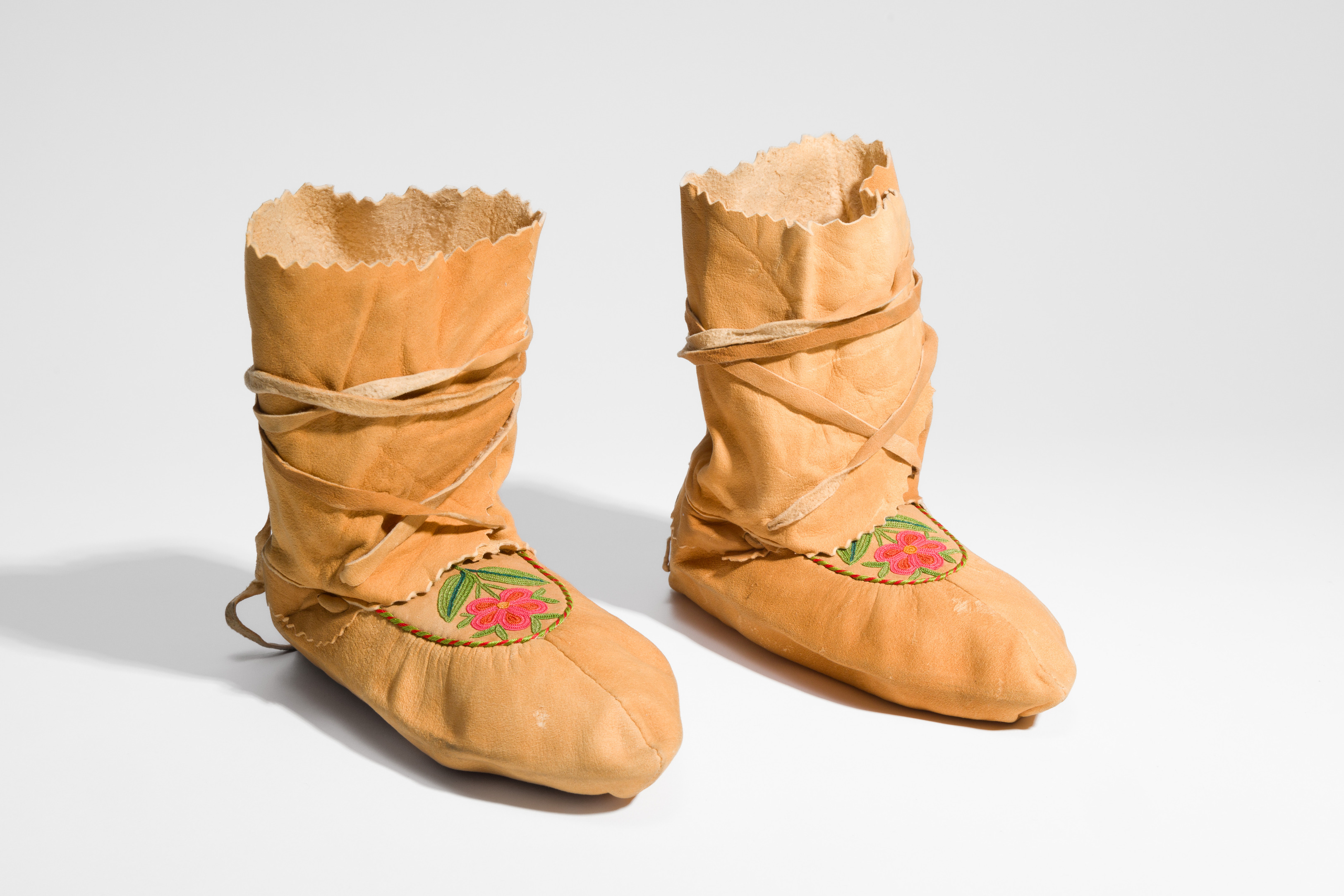 Pair of moccasins with flowers embroidered on the tongues. Shoe extends halfway to calf and is tied with leather laces.