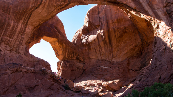 Visitors explore underneath several large rock arches in the desert. 