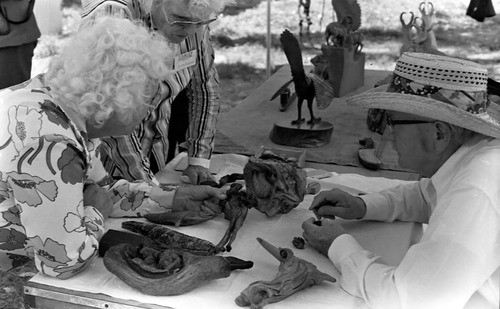 Bill Miller carving a peach pit creature and talking with two women at the first annual Folklife Festival, Zion National Park Nature Center, September 1977.