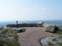 A paved walkway, stone walls, and interpretive markers define the observation point, overlooking hazy flat land.