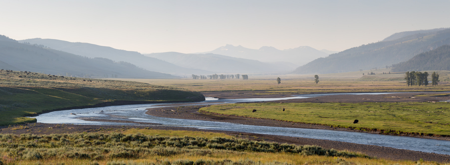 a river runs through a wide open valley with mountains surrounding it.