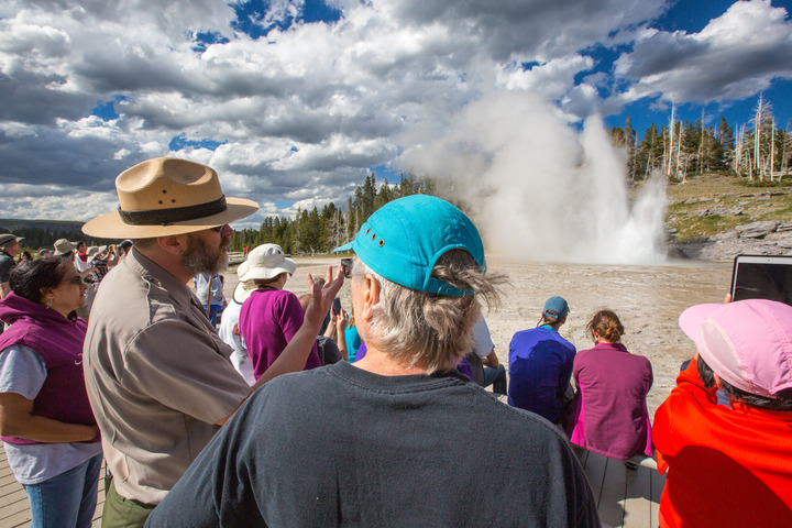 Ranger talks to one person in a crowd of people who watch a geyser erupt
