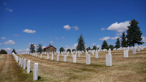 Beyond rows of marble headstones and short, dormant turf, the stone Superintendent's House and conifer trees of the designed landscape stand against the skyline.