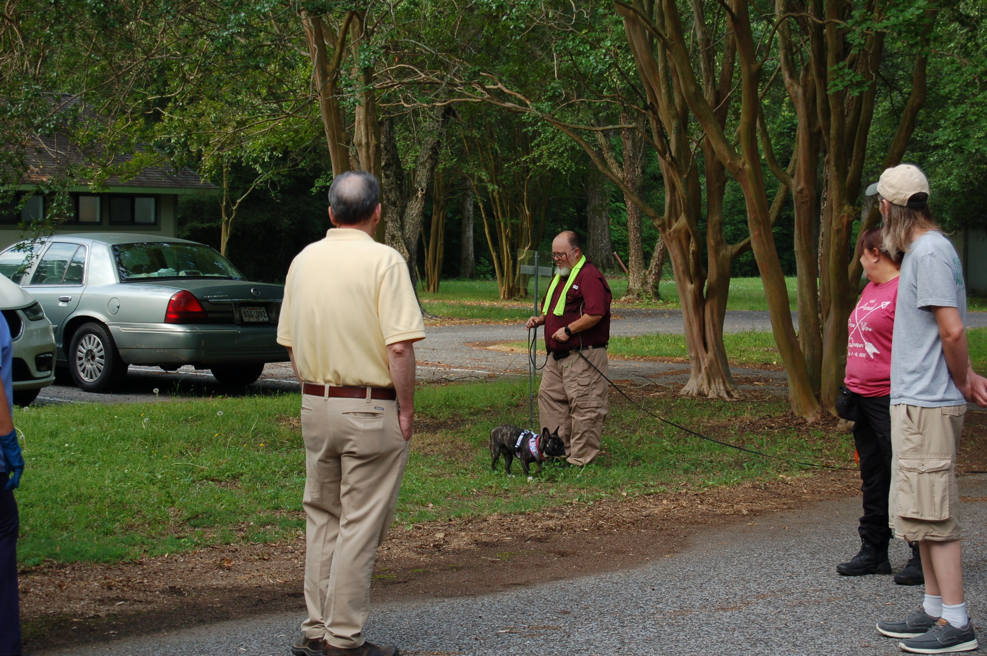 A group of people watch a man holding a small dog on a leash.