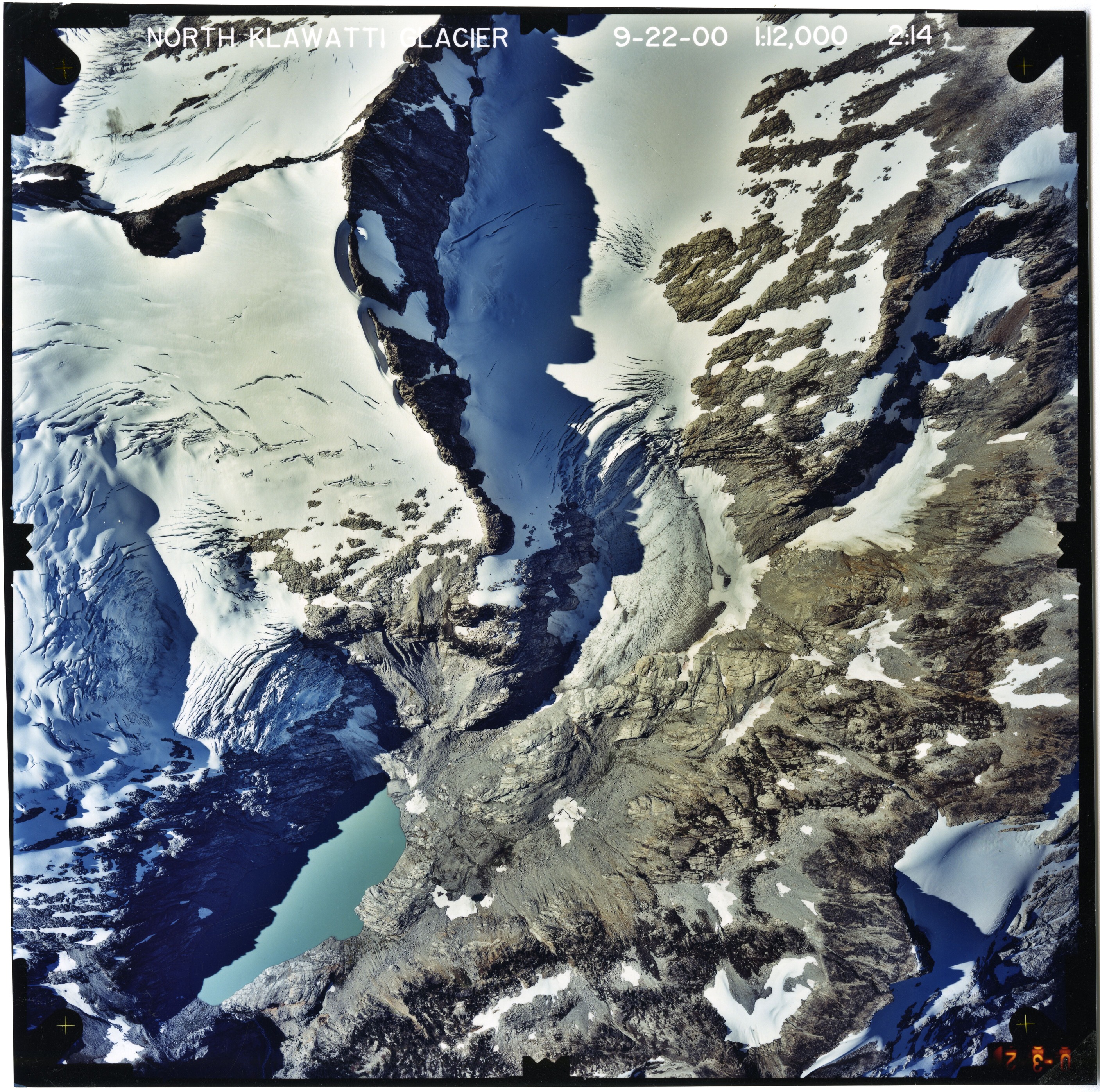 Color aerial photograph of glacier, snowfields, and alpine lake on mountain peak.