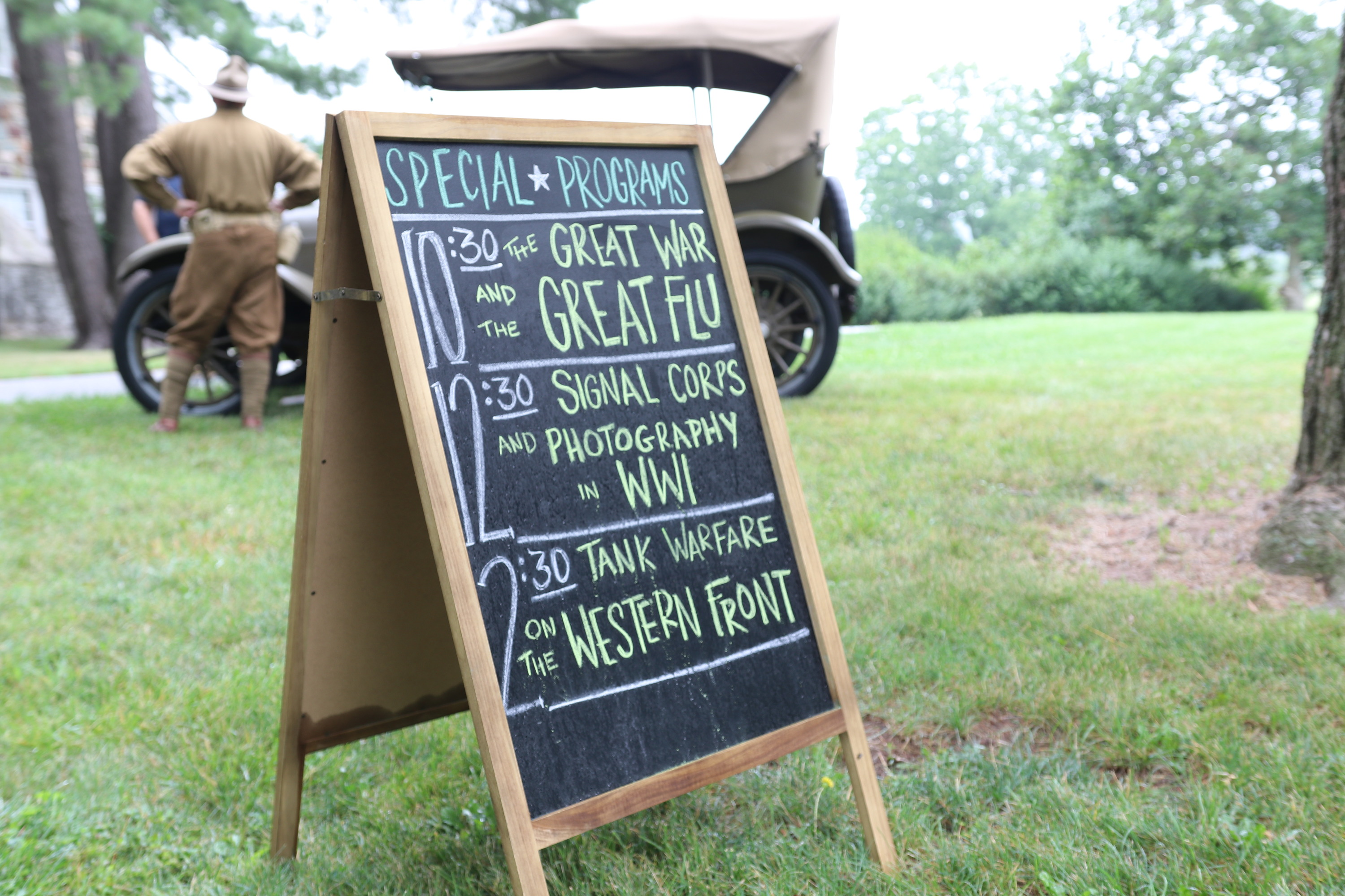 A chalkboard sign and event schedule with a green army car in the background