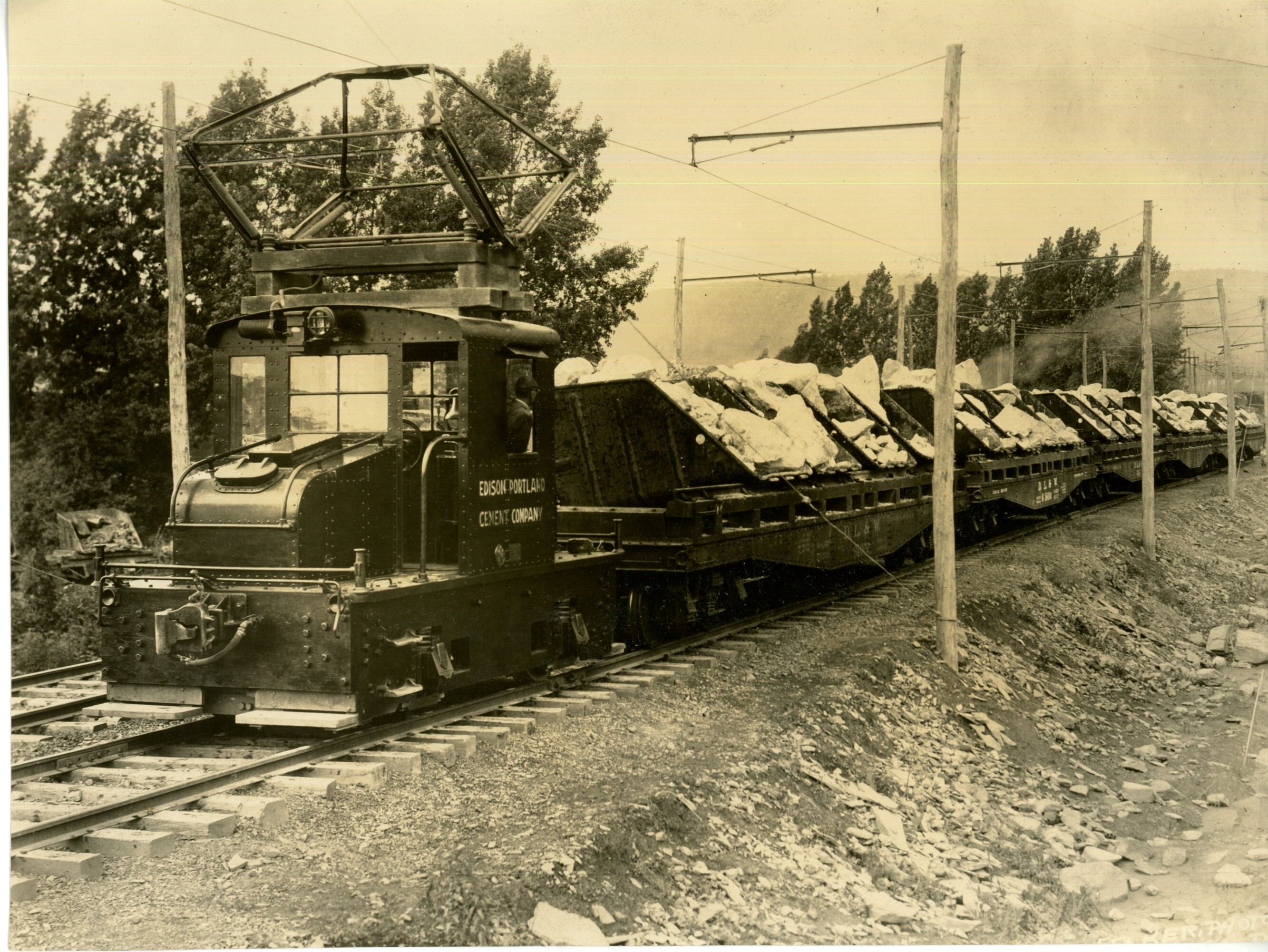 Railway: electric train of skip (hoist) cars conveying limestone to the grinding rolls. Edison Portland Cement Company written on side of train.