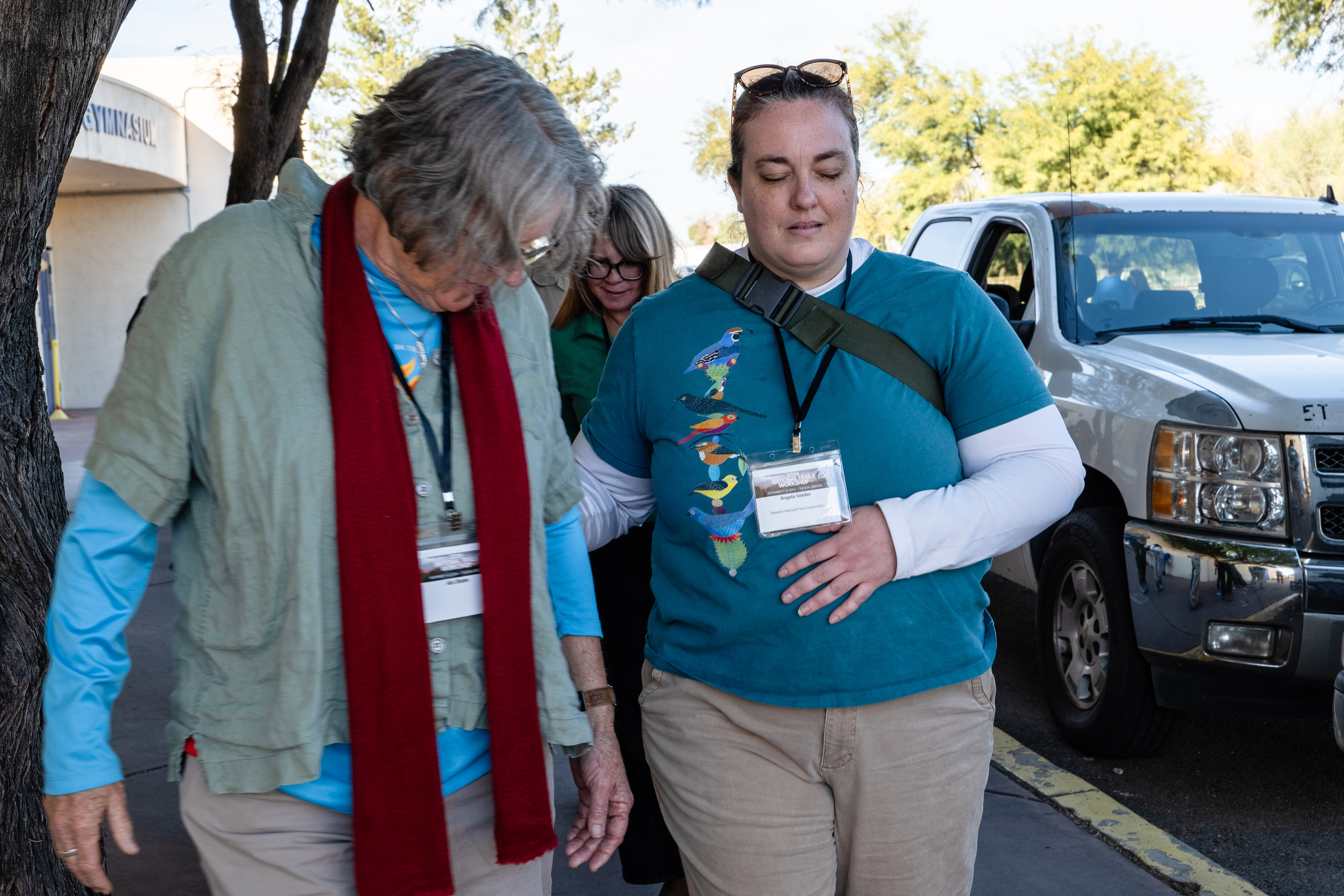 A woman closes her eyes as she's led down a sidewalk