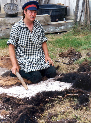 A man in historic dress kneels on the ground with a buffalo hide