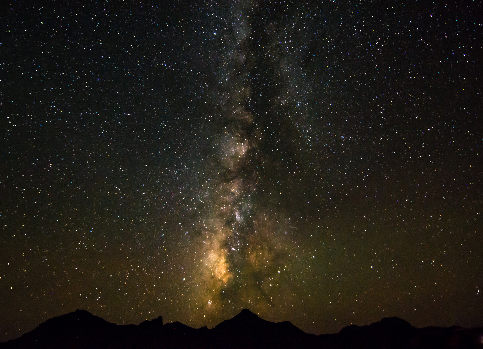 The glow of the Milky Way backlights the silhouette of a mountain range.