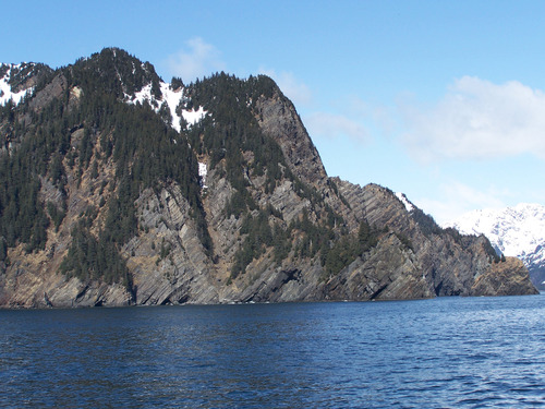 open water with shoreline cliffs in the distance showing tilted layers of rock