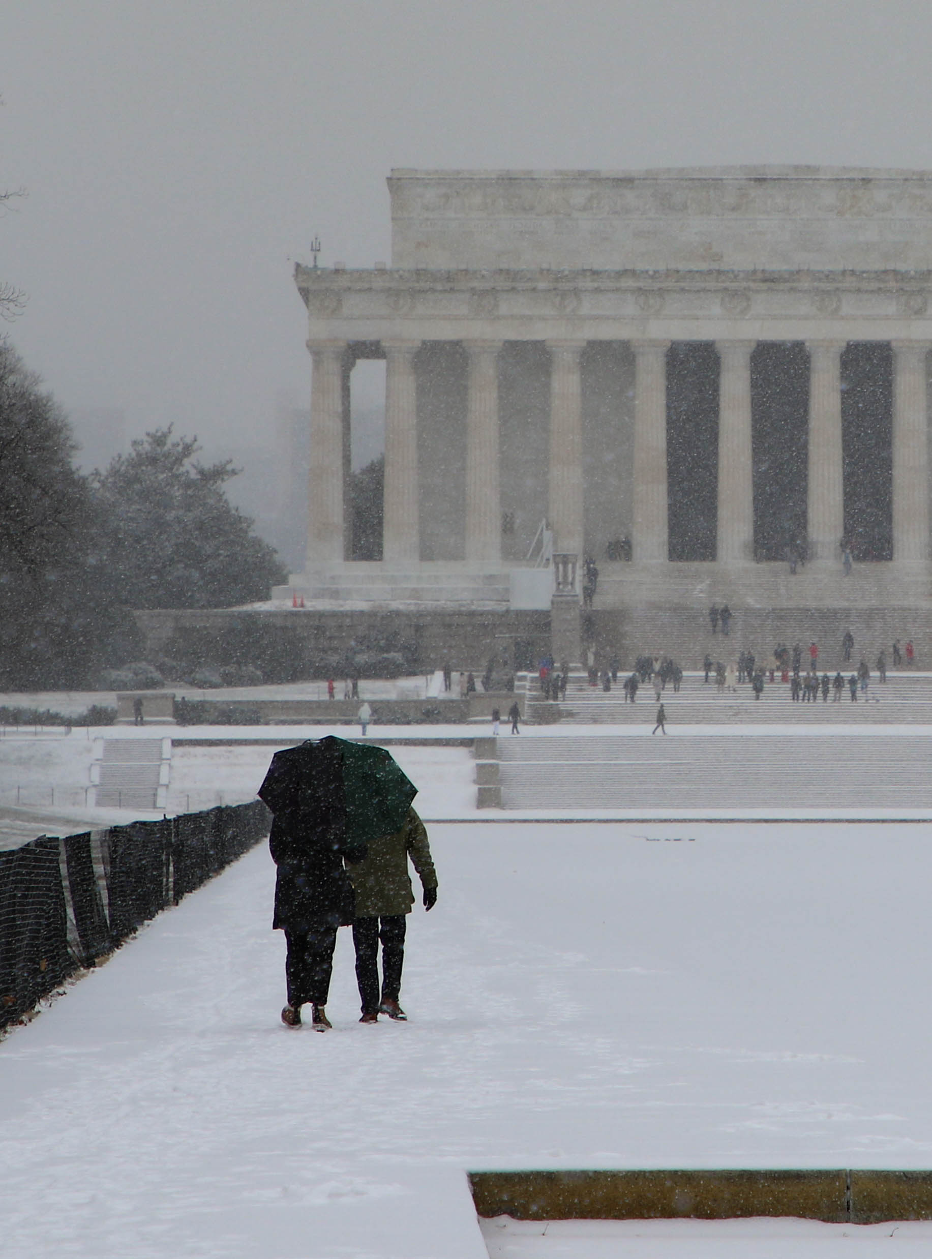 Visitors holding an umbrella walking towards the Lincoln Memorial during a snowfall 