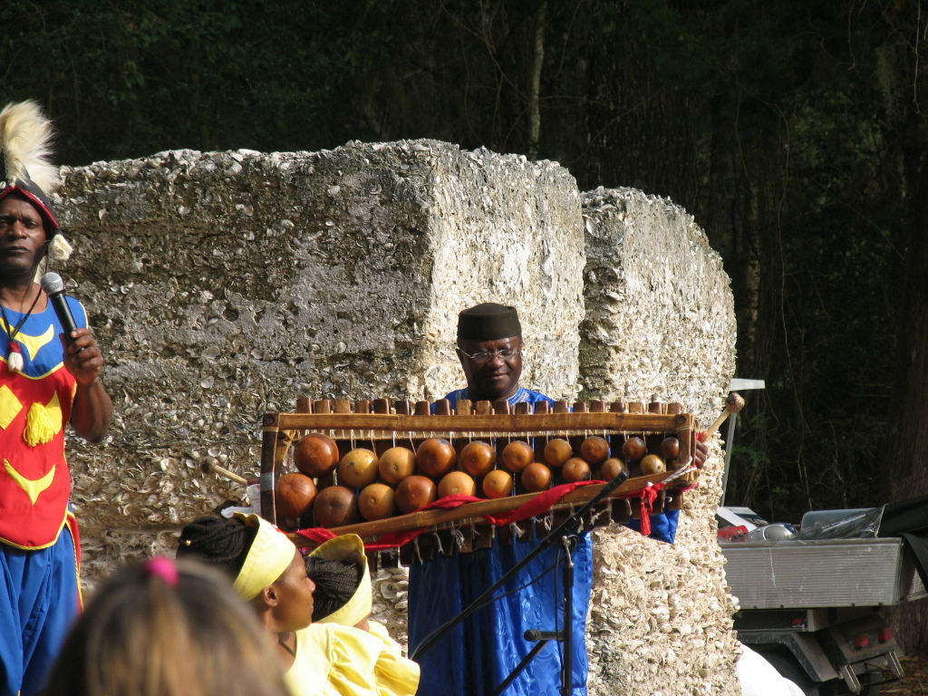 . a man wearing blue holds up a xylophone like instrument made from gourds