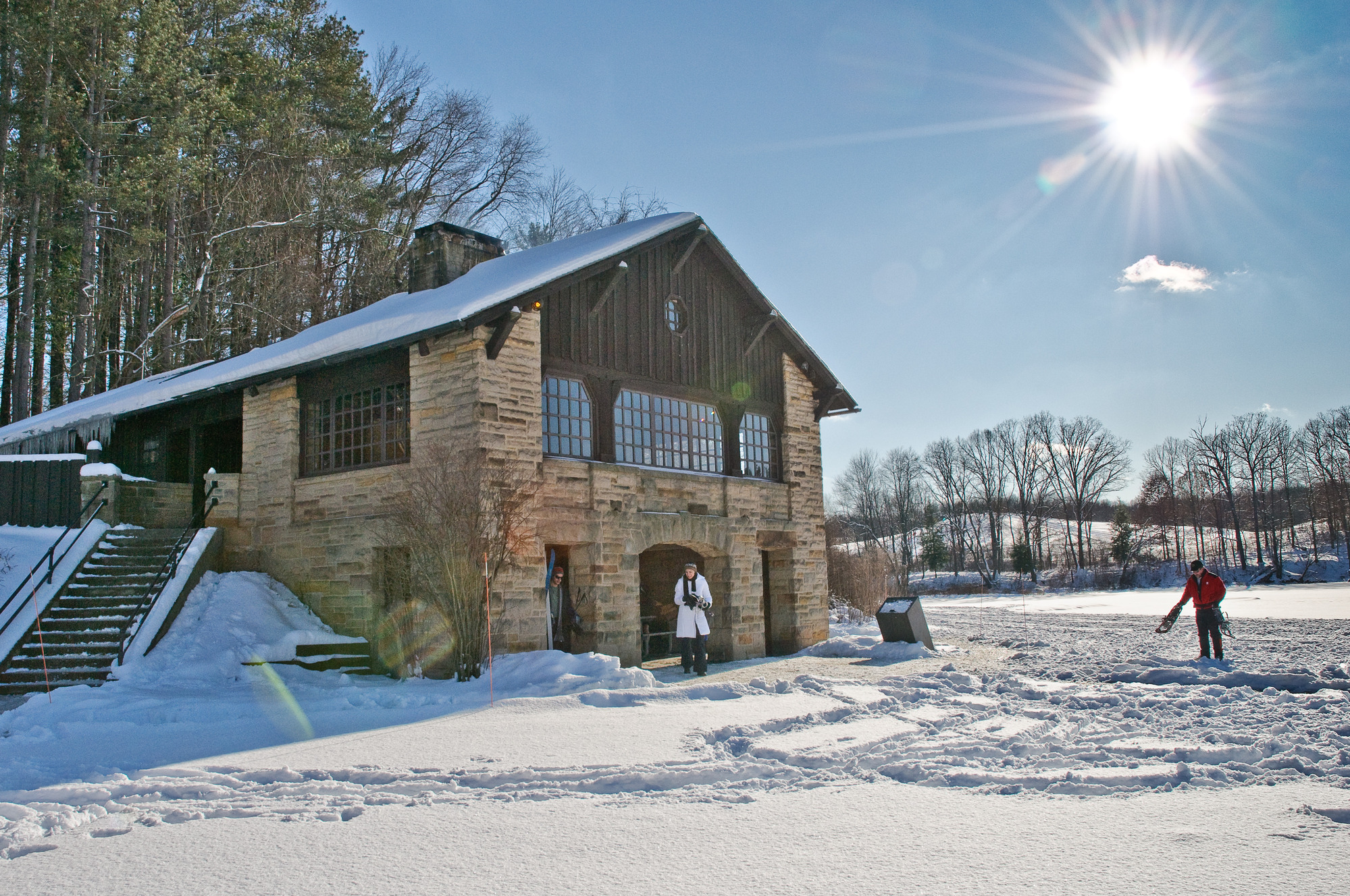 A two-story stone building with arched entryway on the ground floor, on a sunny winter day with snow on the ground around it.