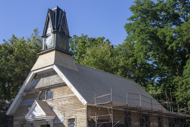 A church in front of late summer trees with fresh siding and scaffolding along the side.