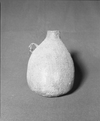Mrs. Donald Segerstrom Collection. Object: Paiute water jug. Dimensions: 11 1/2" height. Materials: Willow, pitch, horsehair. Technology: Start in three strand twining, body in diagonal twining with two bands of plain twining on paired warps in body and one row of three strand twining near neck; pitch applied messily, needles and duff in pitch coating. Photographed by Michael Dixon. Catalogued by Craig Bates and Barbara Beroza. Yosemite Collections, National Park Service. 1/83.