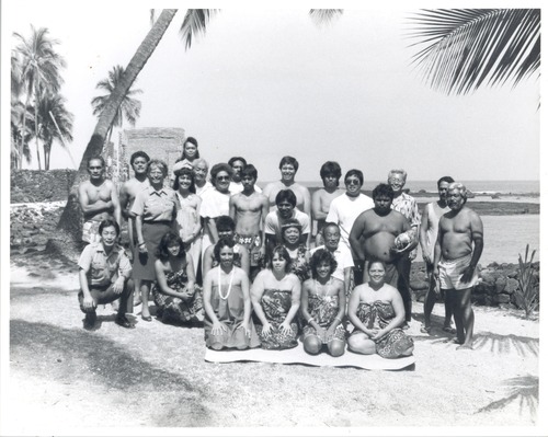 NPS staff, some in uniforms and some in traditional clothing, gather together for a group picture with Hale o Keawe in the background