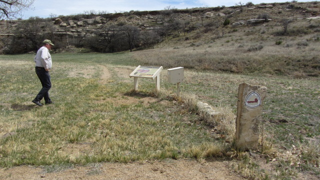 A man standing next to a sign in a grassy field.
