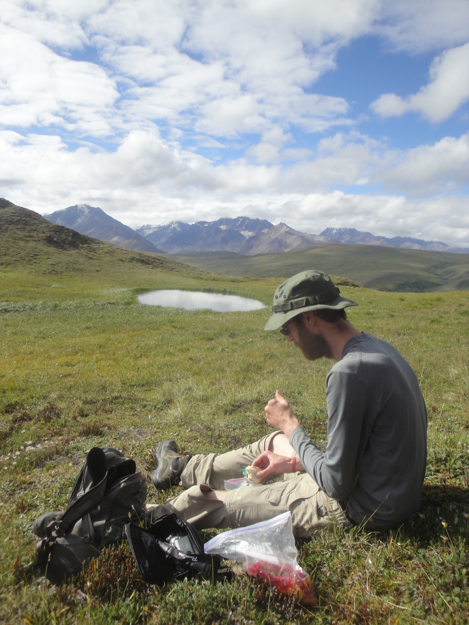 man sitting in an alpine meadow eating a snack