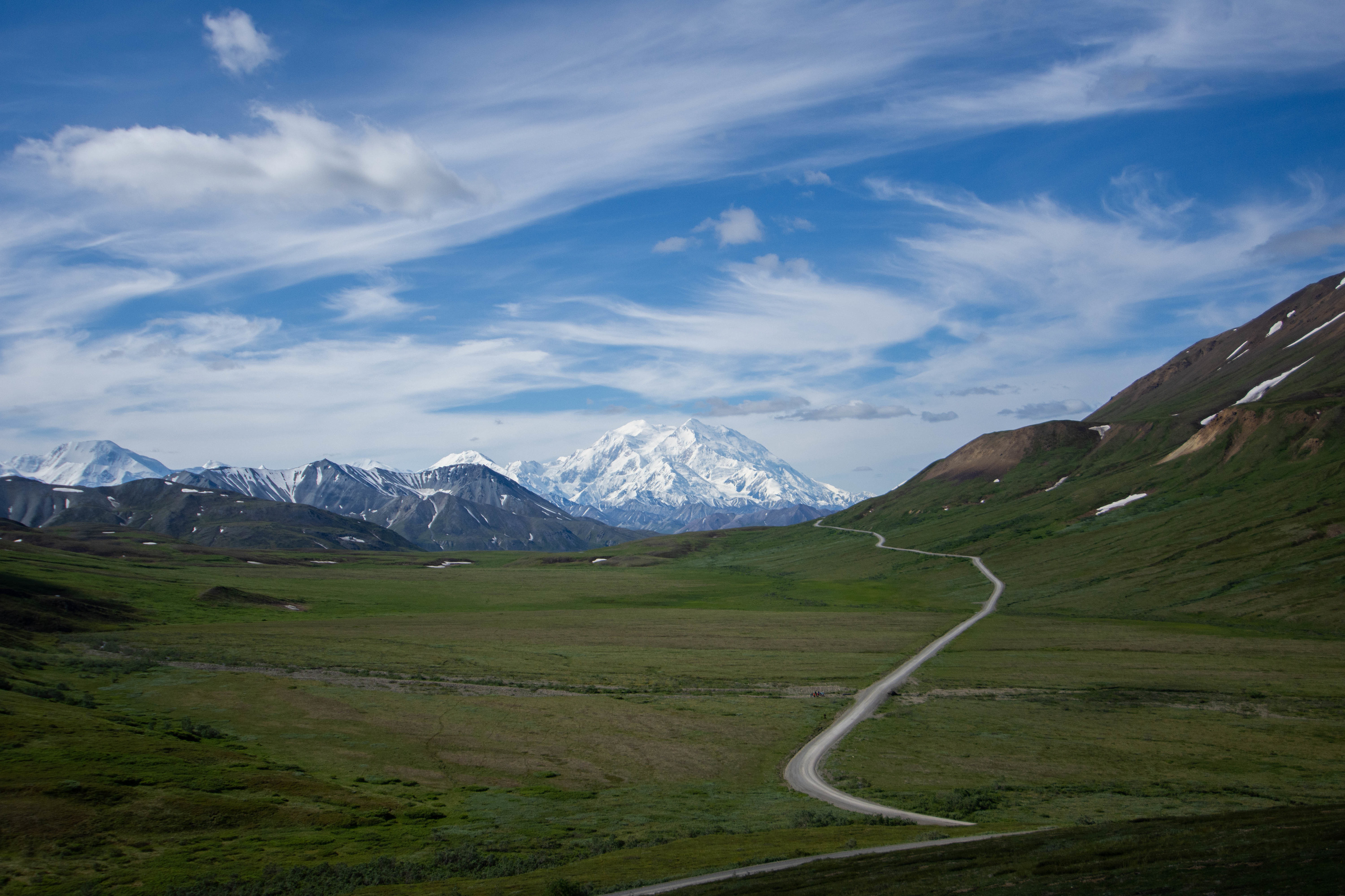 a dirt road leading through mountainous landscape toward a huge, snowy mountain