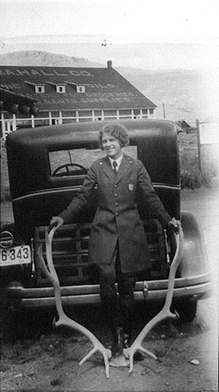Ranger Frances Eva Pound in her Park Service uniform stands in front of a car, holding onto large antlers.