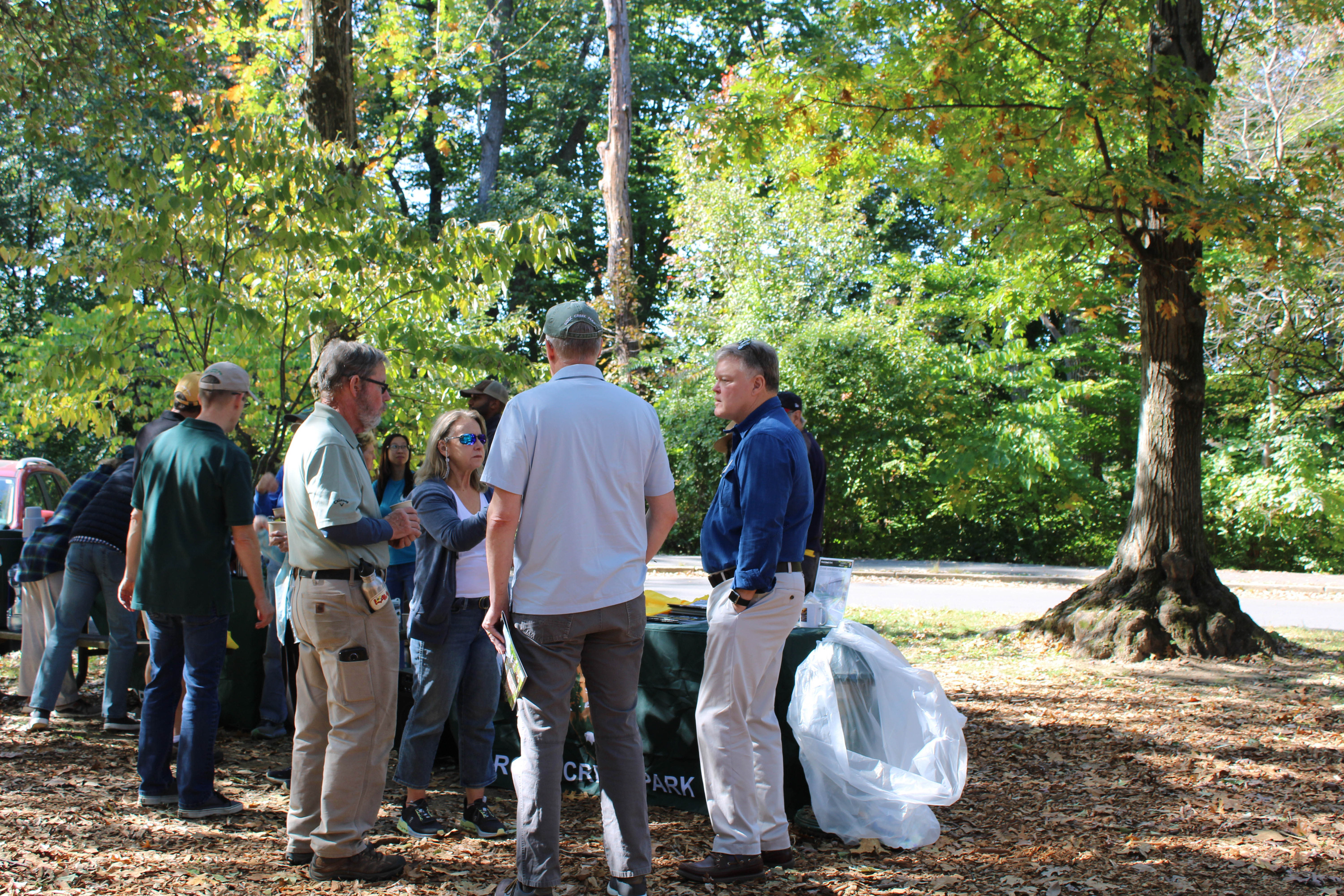 A group of volunteers chatting with one another in an outdoor picnic grove in front of a National Park Service table.