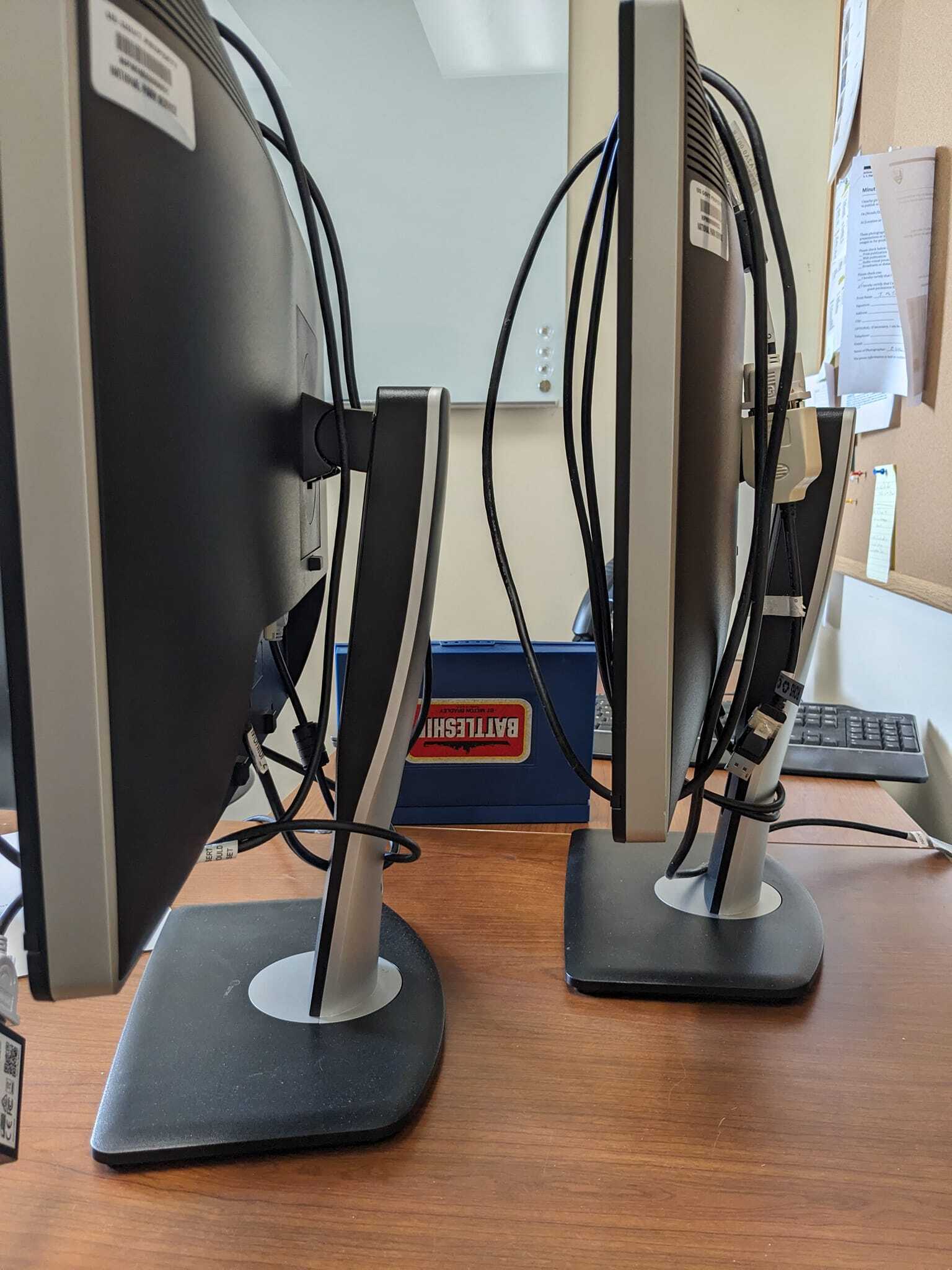 On a desk behind two computer monitors, a battleship board is hidden