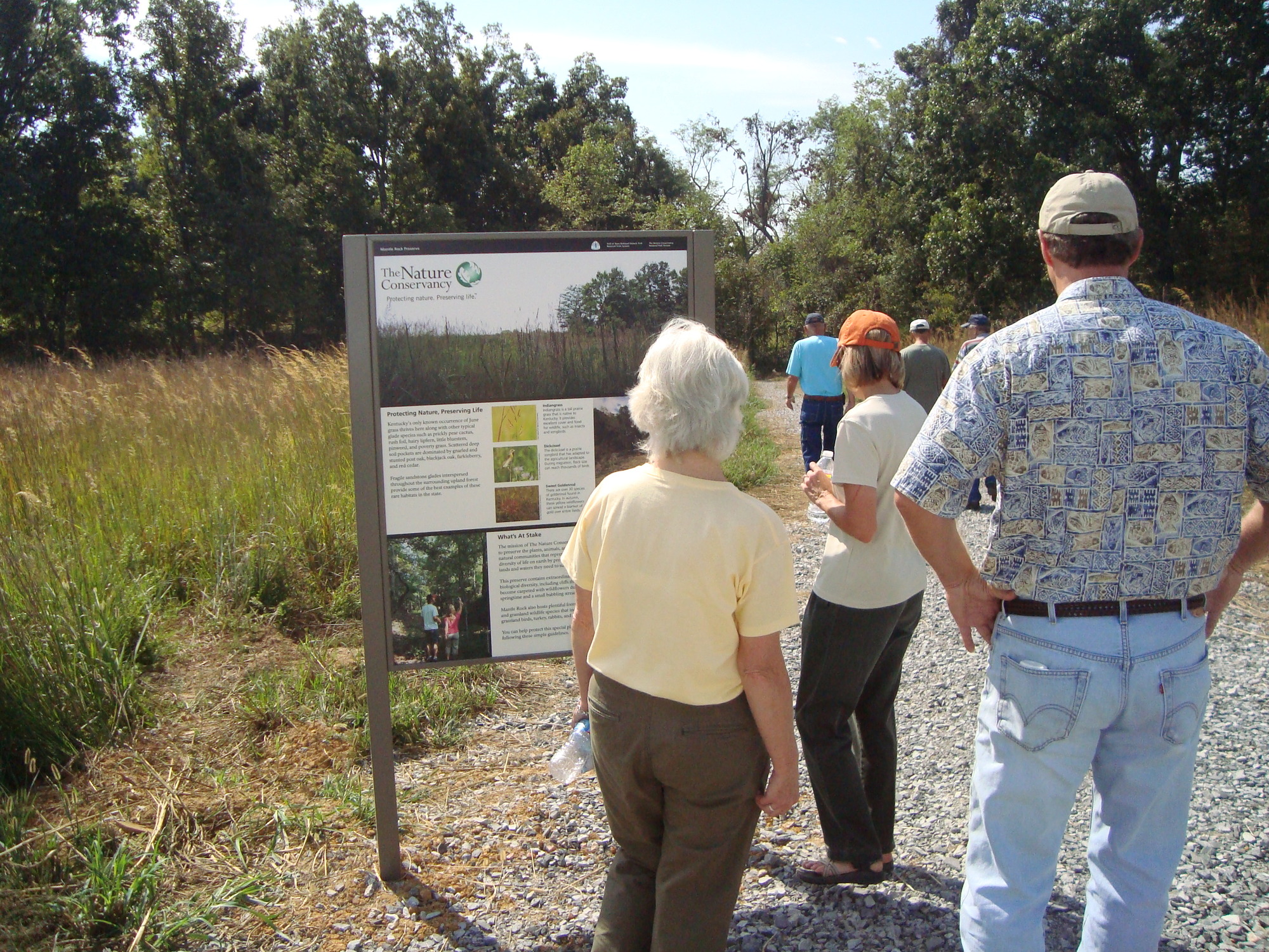 A group of people looking at a sign in a wooded area.