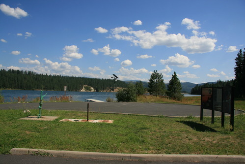 Color photograph of a paved parking area and grassy area with sign next to a lake