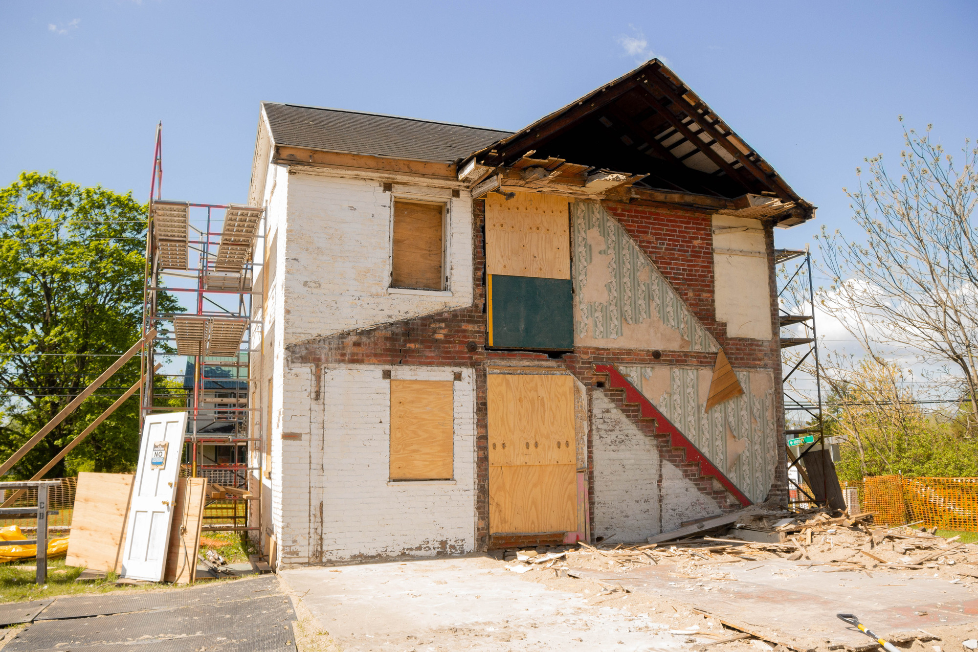 The back of a home with damage and debris is shown exposing the inside with leftover imprints from stairs and wallpaper. 