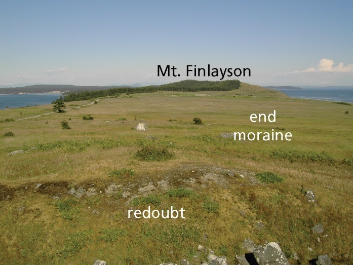 Photo of a hilltop prairie with forested slopes and open water in the distance.