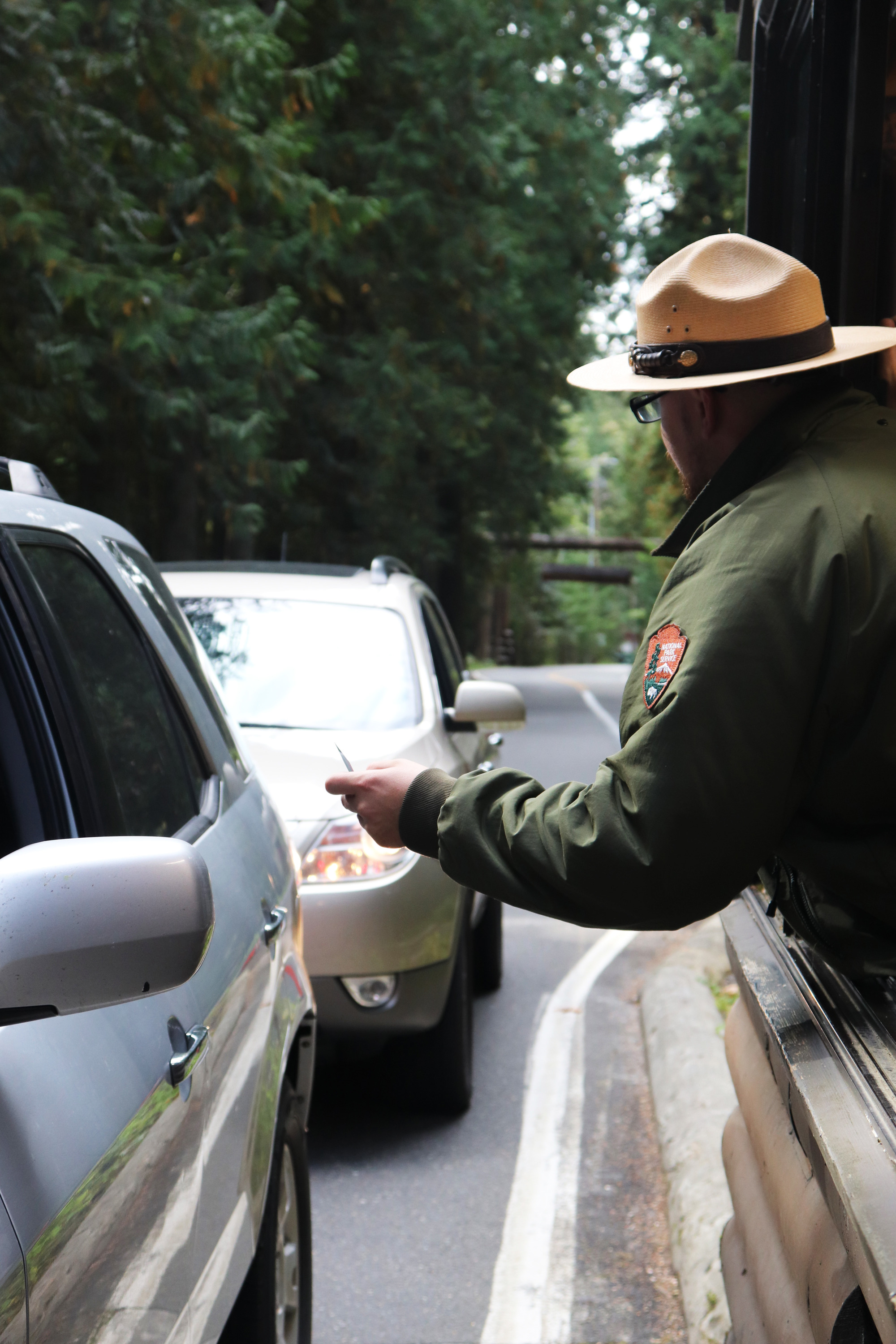 A ranger leans out of an entrance booth to hand a card to someone in a car.