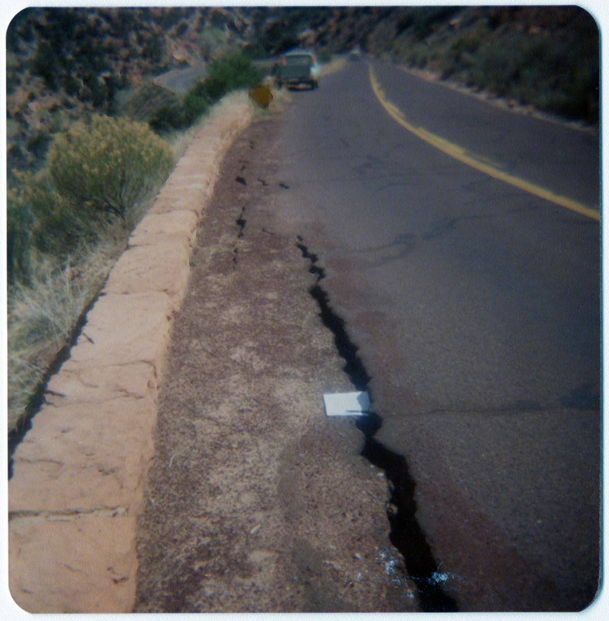 Crack in road in need of repair with paper marking over top.