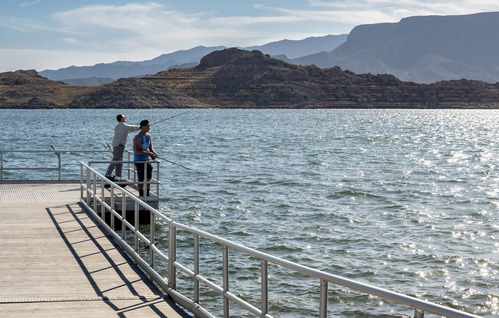 Fishing pier extending into lake, two active fishermen, mountains in background