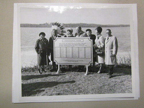 Seven people standing behind the new sign on the shoreline. The Potomac River is in the background.