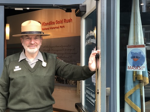A smiling park ranger standing and holding open a door.
