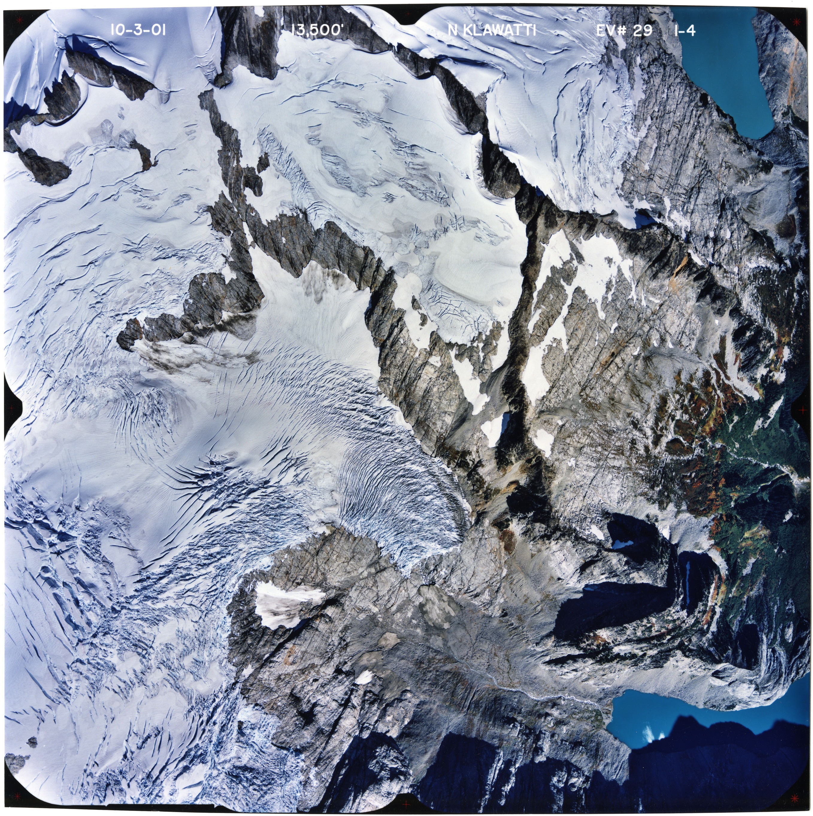 Color aerial photograph of glacier, snowfields, and alpine lake on mountain peak.