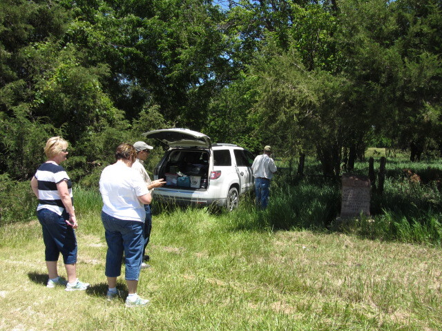 A group of people standing near a car in a field.