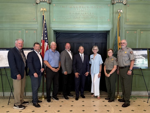 A group of eight people post inside of a building with tile floor and wood panneled rooms.