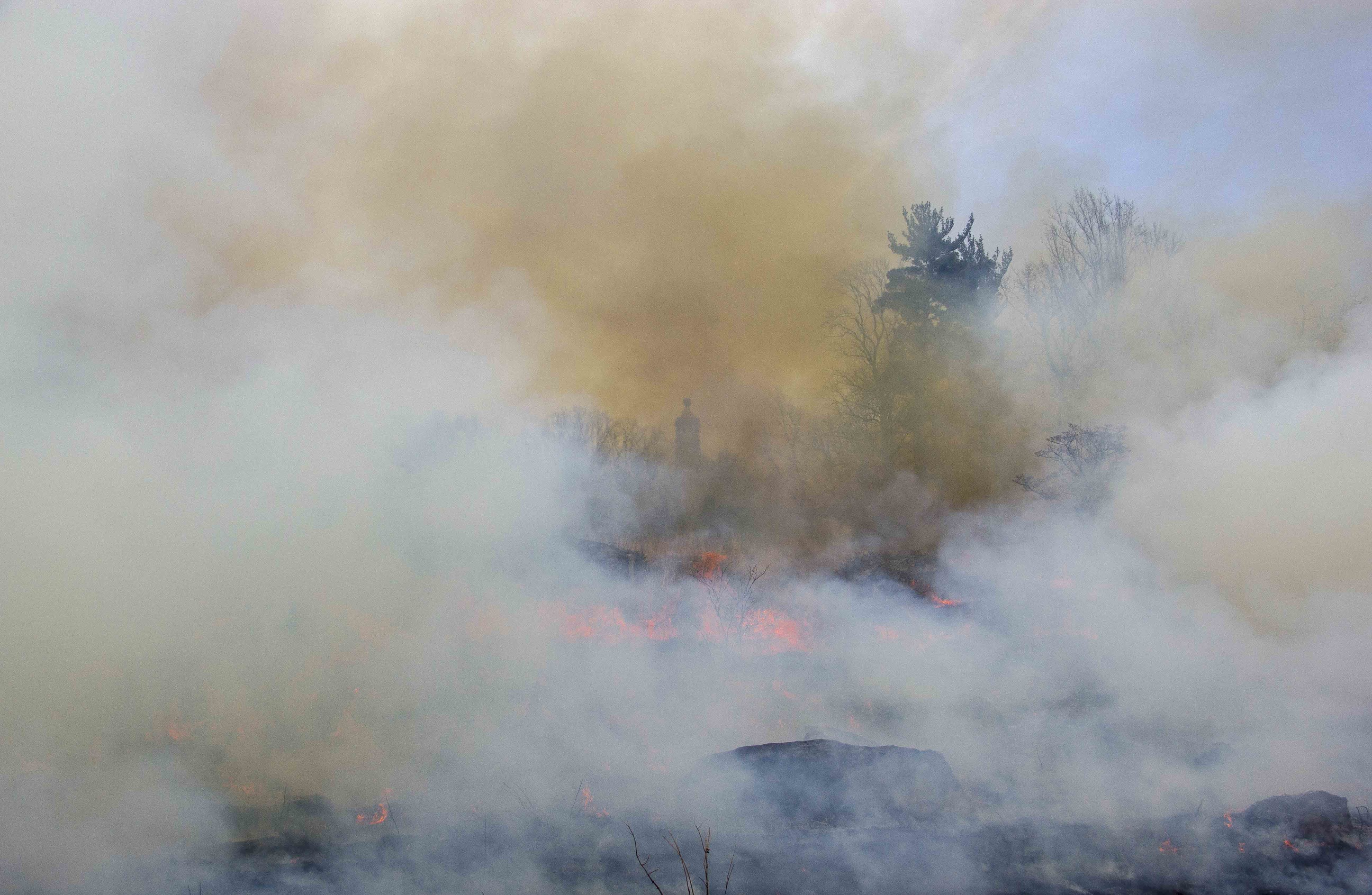 The prescribed fire reaches its apex. Heavy smoke nearly obscures the 44th New York monument in the distance. There are a few large boulders in the foreground but the heavy smoke nearly obscures all the features of Little Round Top.