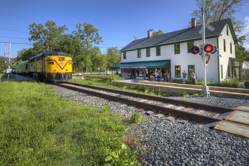 A train approaching a white two-story building with green awning.