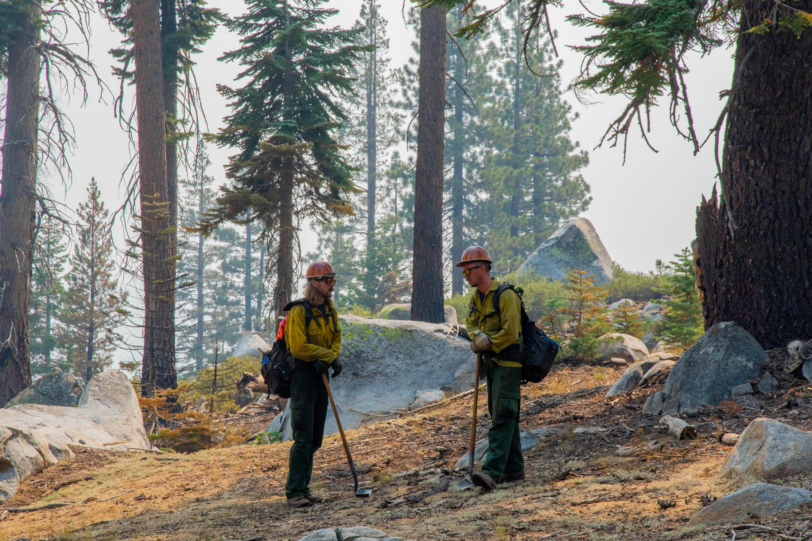 Wildland firefighters walk through wooded areas with smoke and fire around them