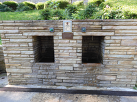 A stone structure with two cut outs which house the jug fountains. There are two buttons to dispense the water, between them is a mineral analysis. 