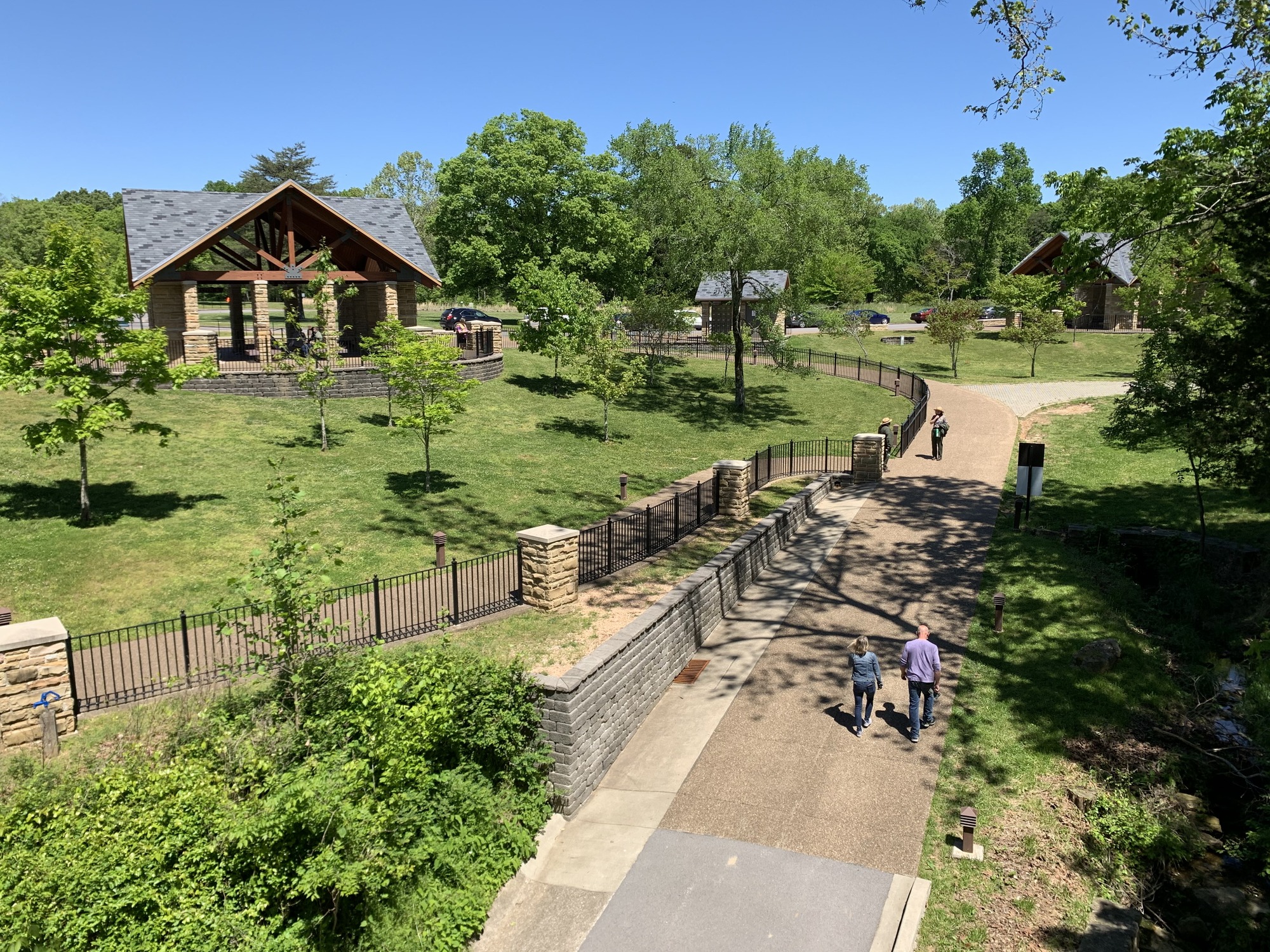 People walking on paved walking trails with small covered shelters in the distance. 