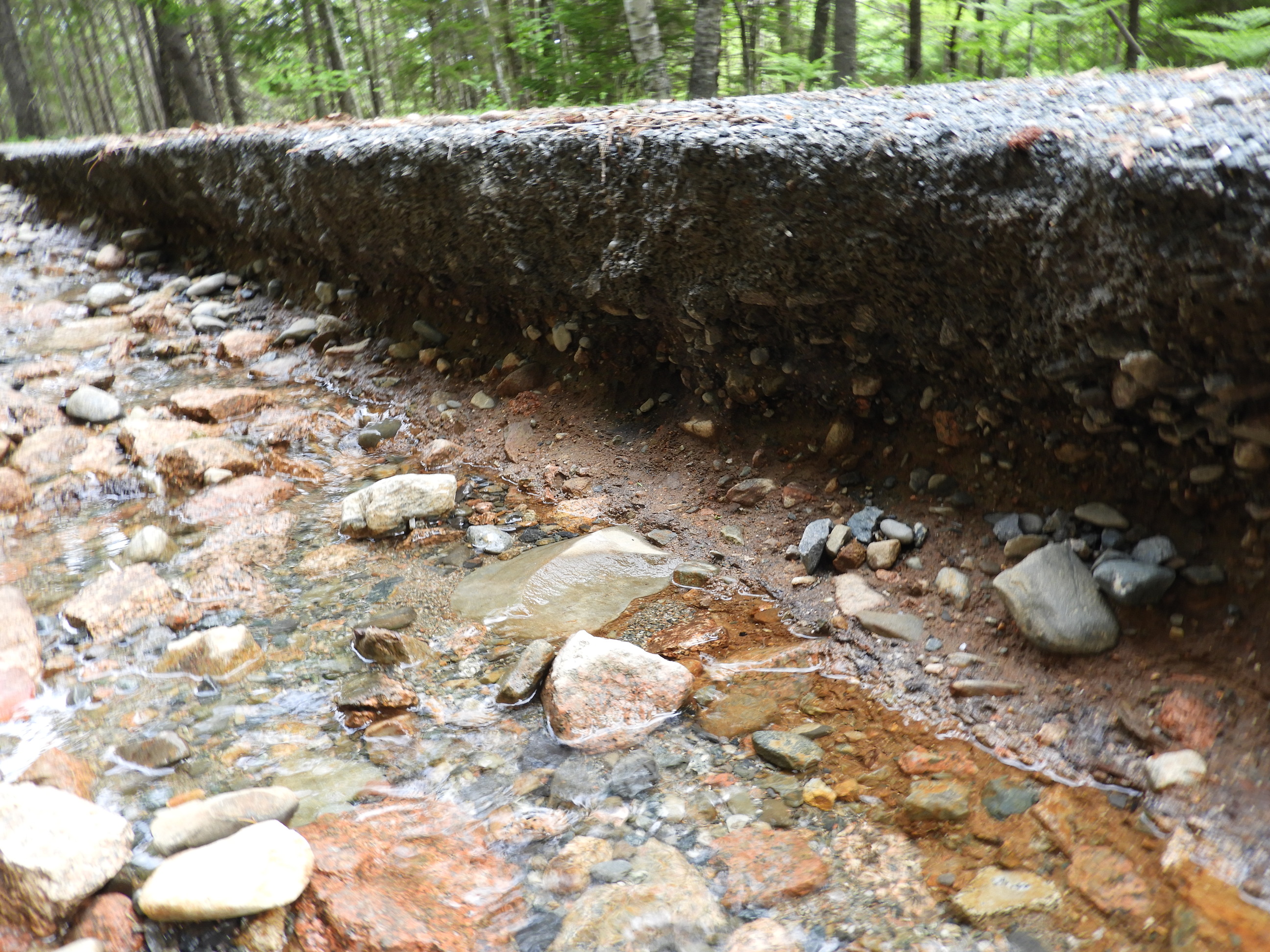 water running downhill in front of washed out road layers 