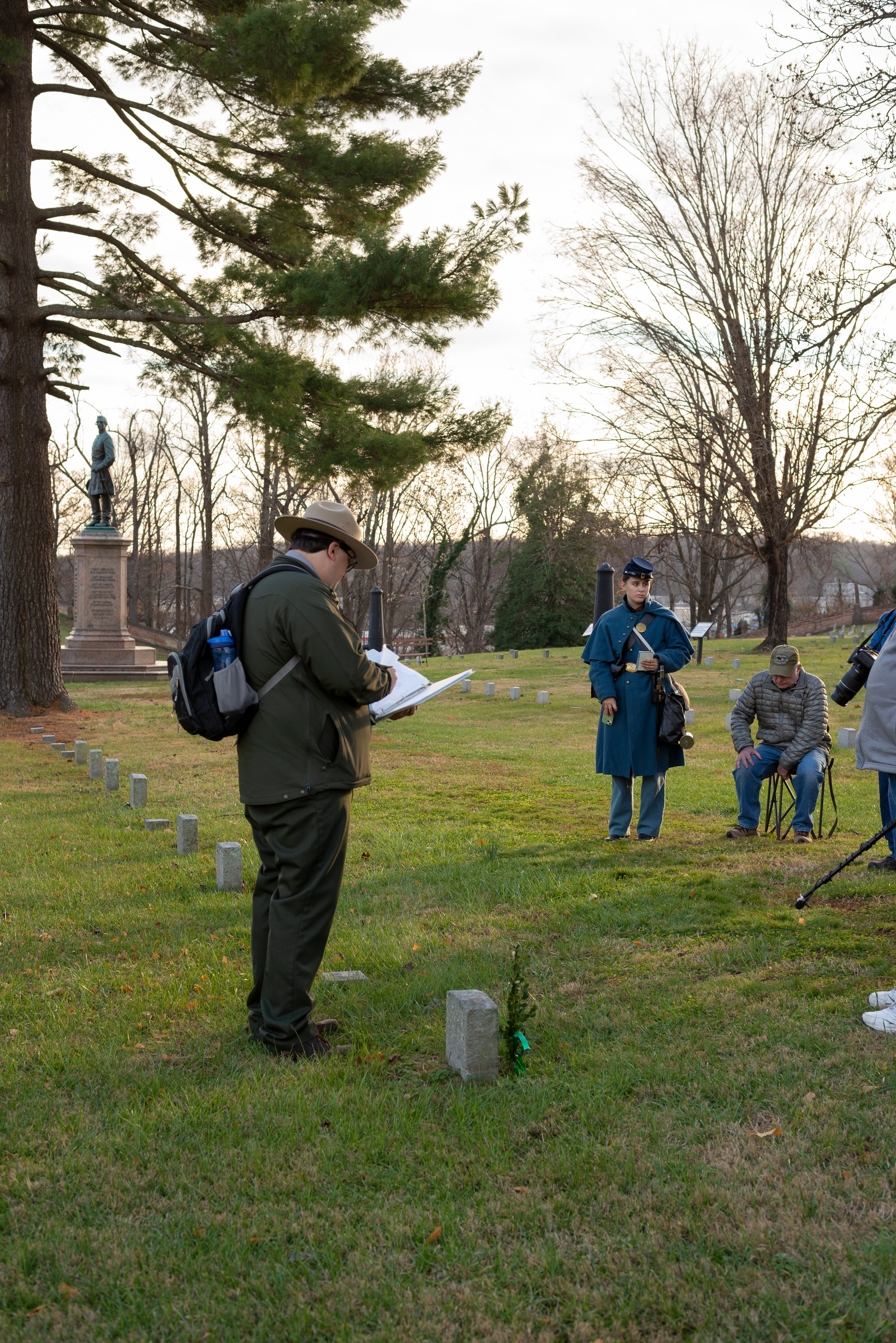 A park ranger speaks to a group of 10 people in a cemetery.