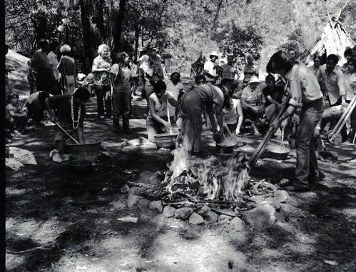 Cooking acorn mush at the Roundhouse Dedication, Yosemite Valley. Craig Bates lifting cooking stones from fire on right, woman cooking acorn mush (L to R): Lucy Parker, (standing Felicia Espina), Kimberly Stevenot, (back to camera, Julia Parker) partially hidden Gael Amend, and hidden behind Craig Bates, Bernie Hopper.