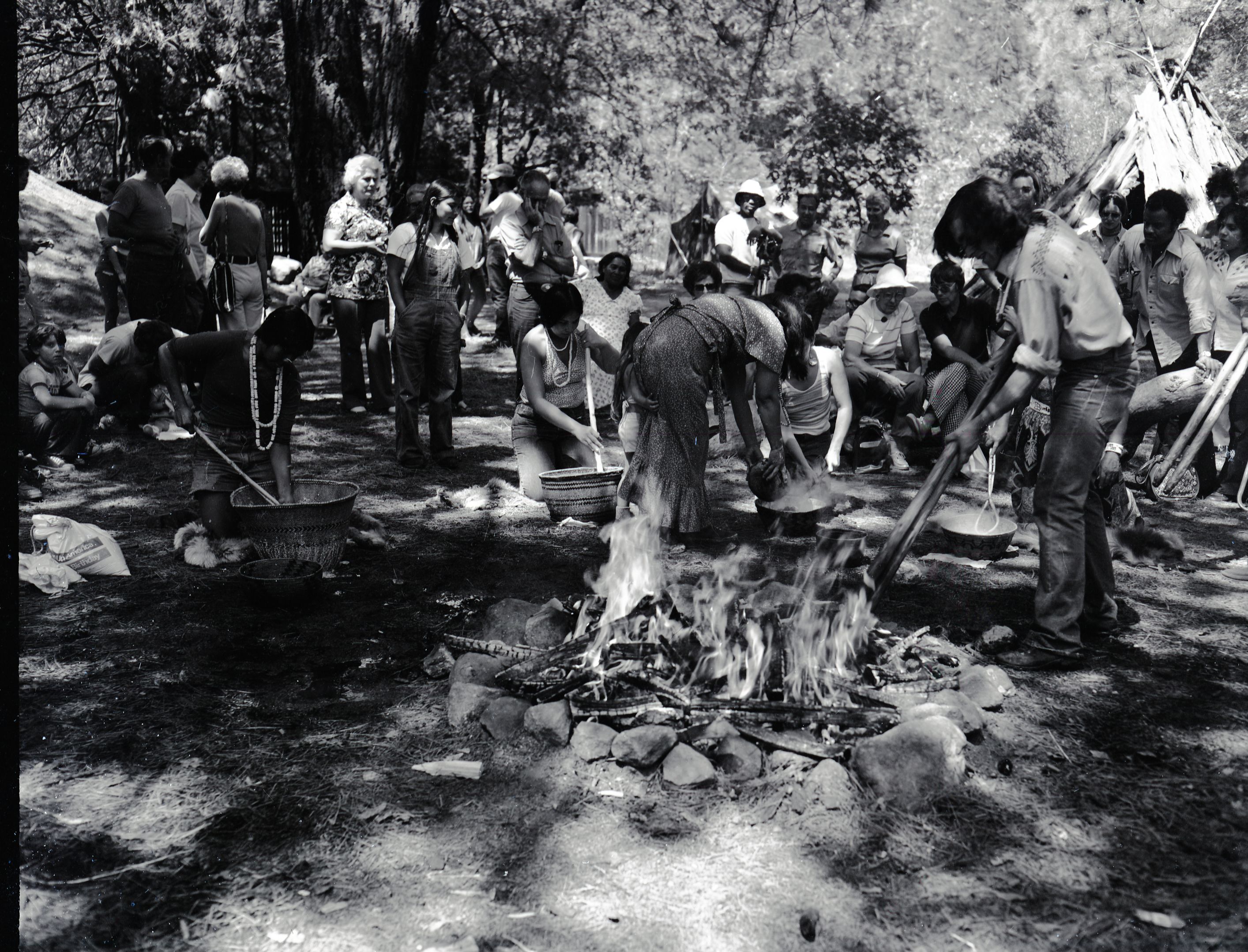 Cooking acorn mush at the Roundhouse Dedication, Yosemite Valley. Craig Bates lifting cooking stones from fire on right, woman cooking acorn mush (L to R): Lucy Parker, (standing Felicia Espina), Kimberly Stevenot, (back to camera, Julia Parker) partially hidden Gael Amend, and hidden behind Craig Bates, Bernie Hopper.