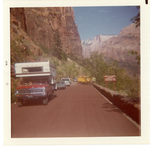 Vehicles driving down road with construction vehicle on opposite side during chipsealing of Zion roads.